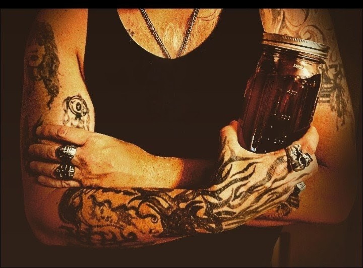 Tattooed arms holding a jar of small-batch spirit