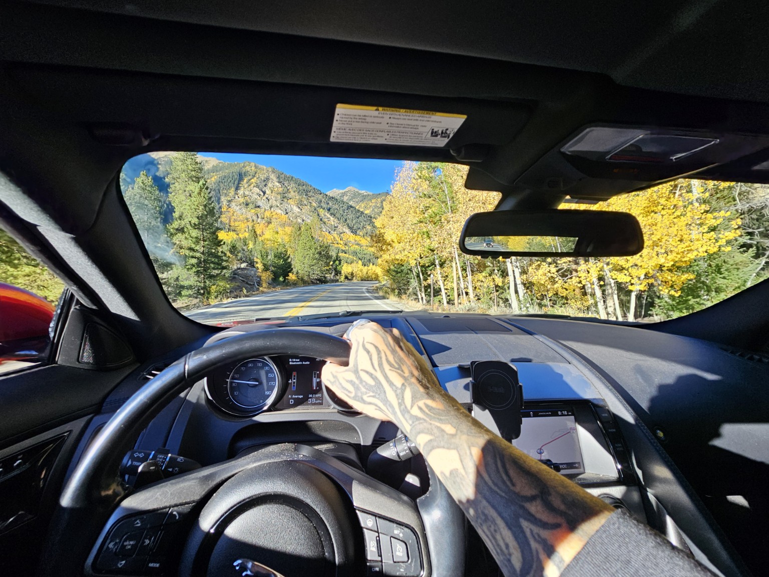 Driving through Colorado mountain roads with yellow aspens, tattooed arm on the wheel